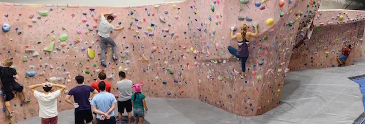 Climbers bouldering above the padded landing surface while friends watch