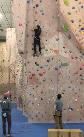 A first-time climber on the wall with a staff member belaying